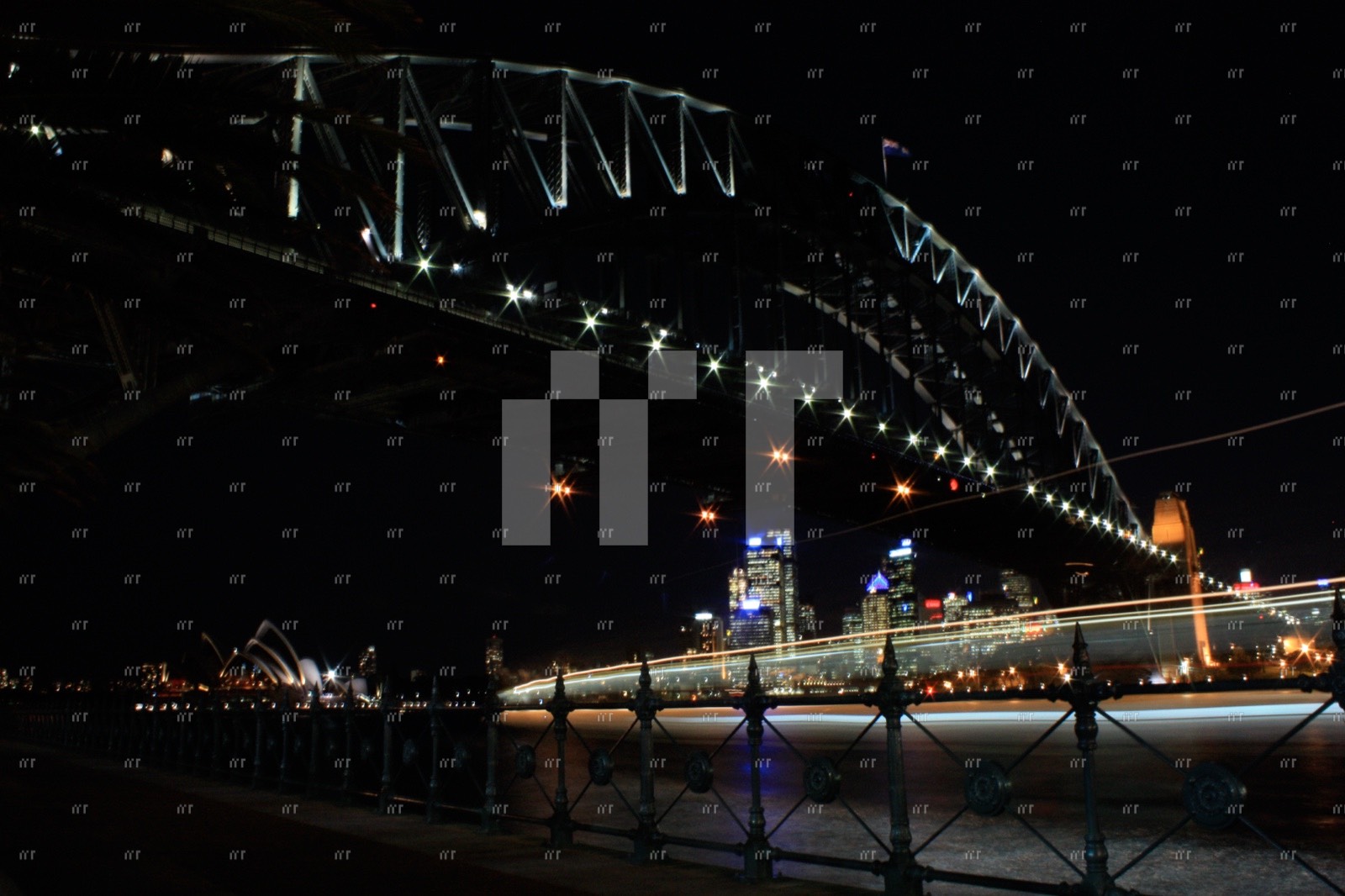 Sydney Harbour Bridge lit up at night from below, the Opera House in the distance and a boat's light trail beneath