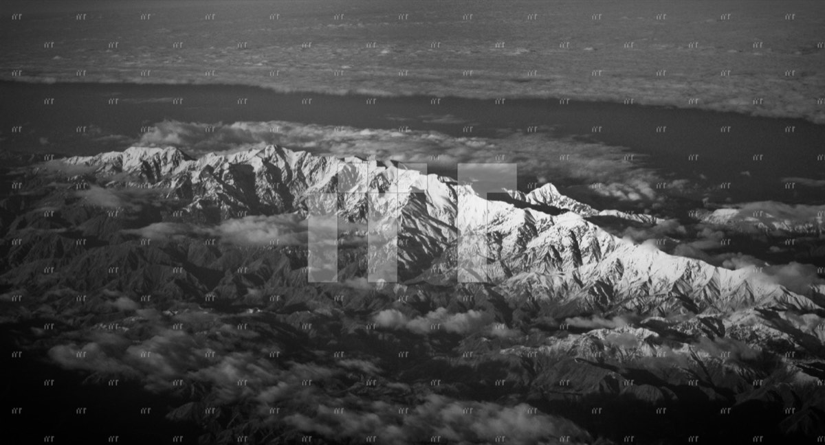 A black and white aerial view of a snow-covered mountain range above cloud