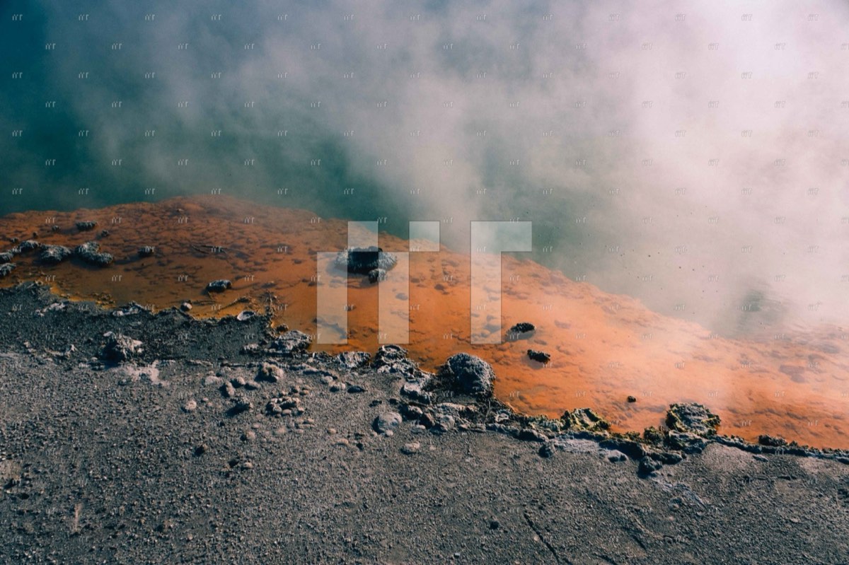 Steam rising from orange-stained rocks at a geothermal pool in Rotorua