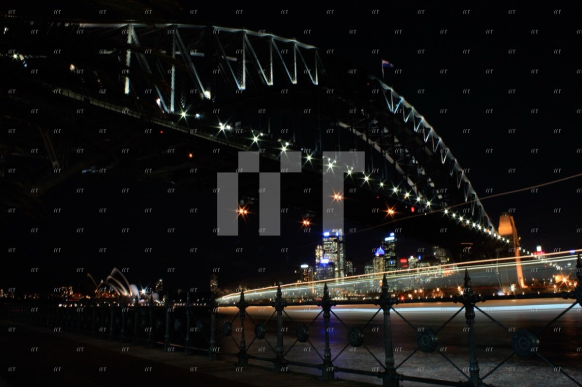 Sydney Harbour Bridge lit up at night from below, the Opera House in the distance and a boat's light trail beneath