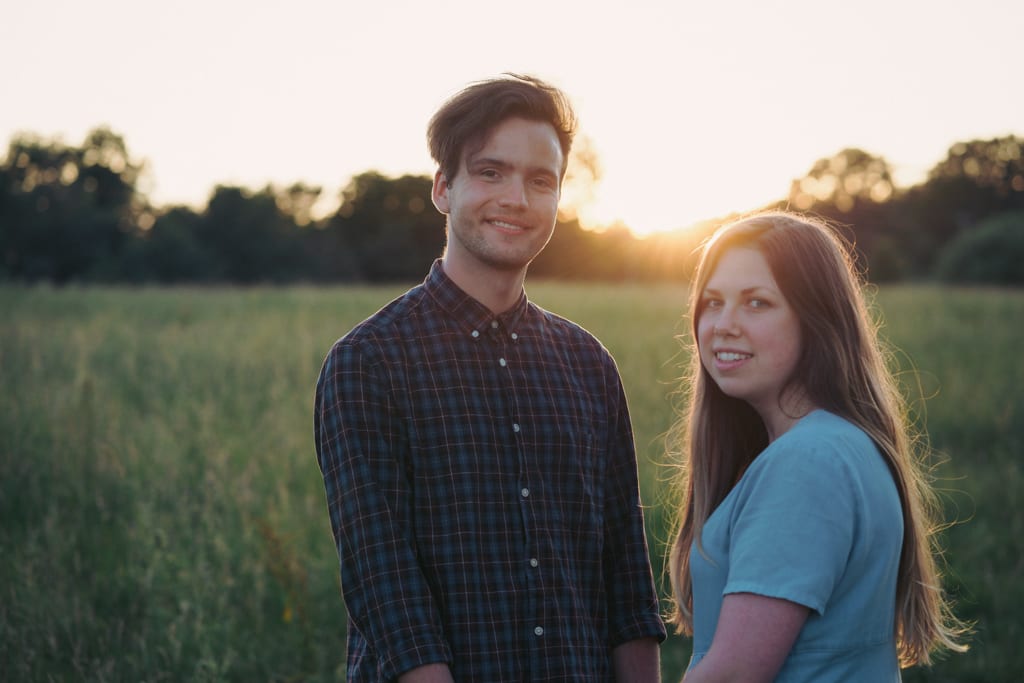 A couple standing close together in a field at sunset