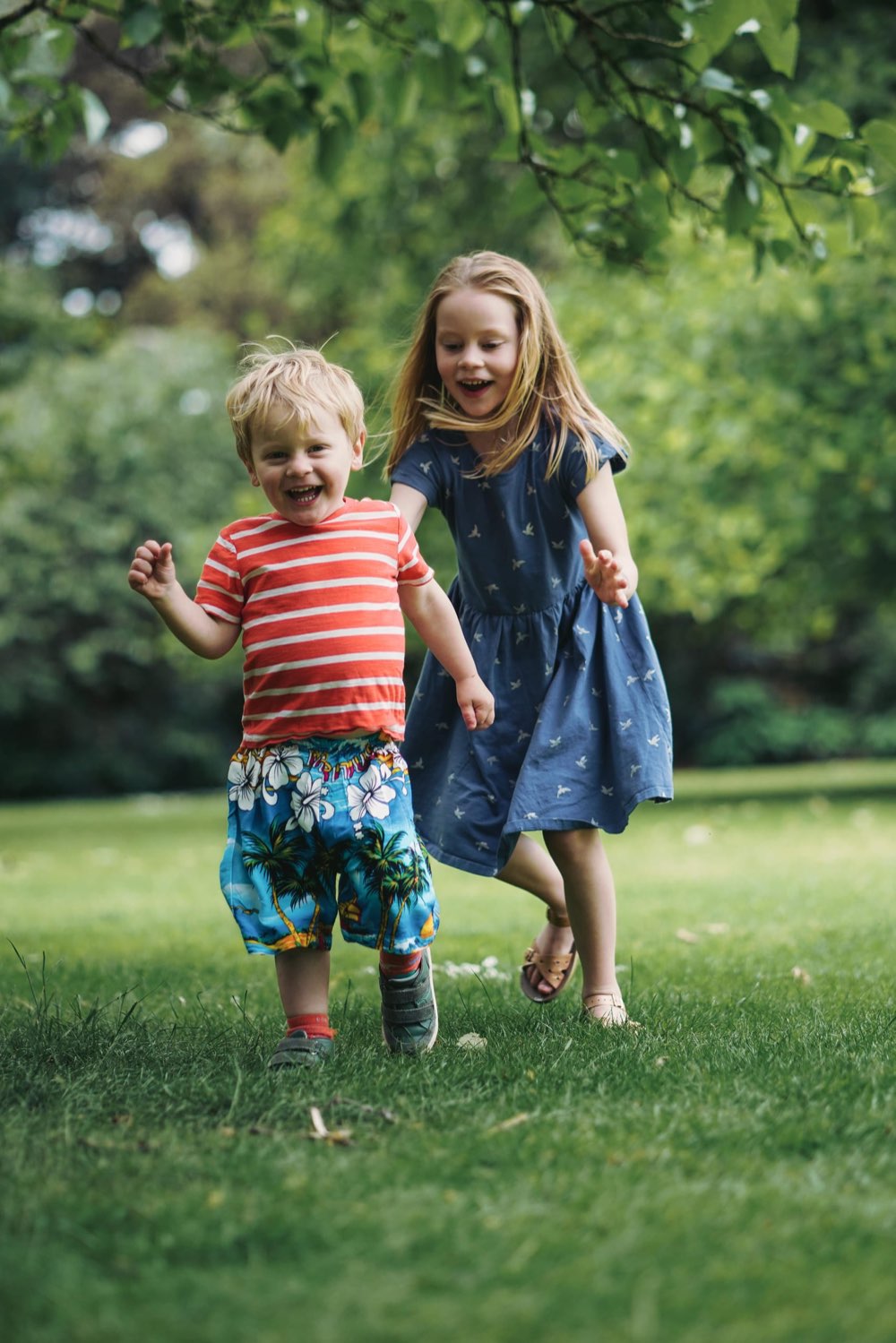 Two children running hand in hand towards the camera across a grassy field