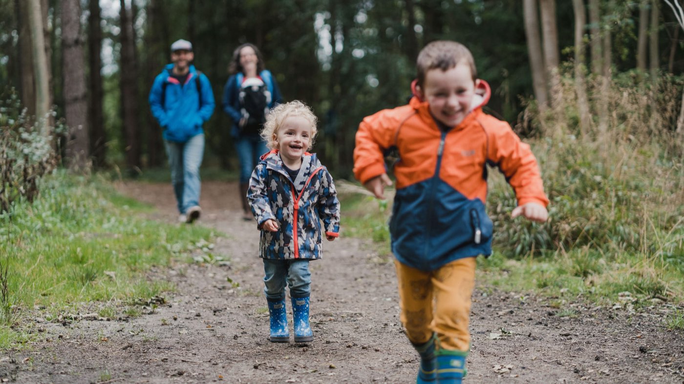 A family walking through woodland while the children run ahead