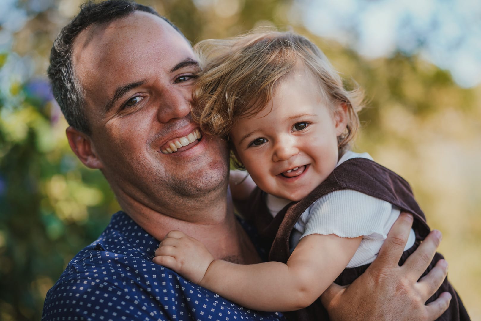A father and his young daughter sitting close together in a garden