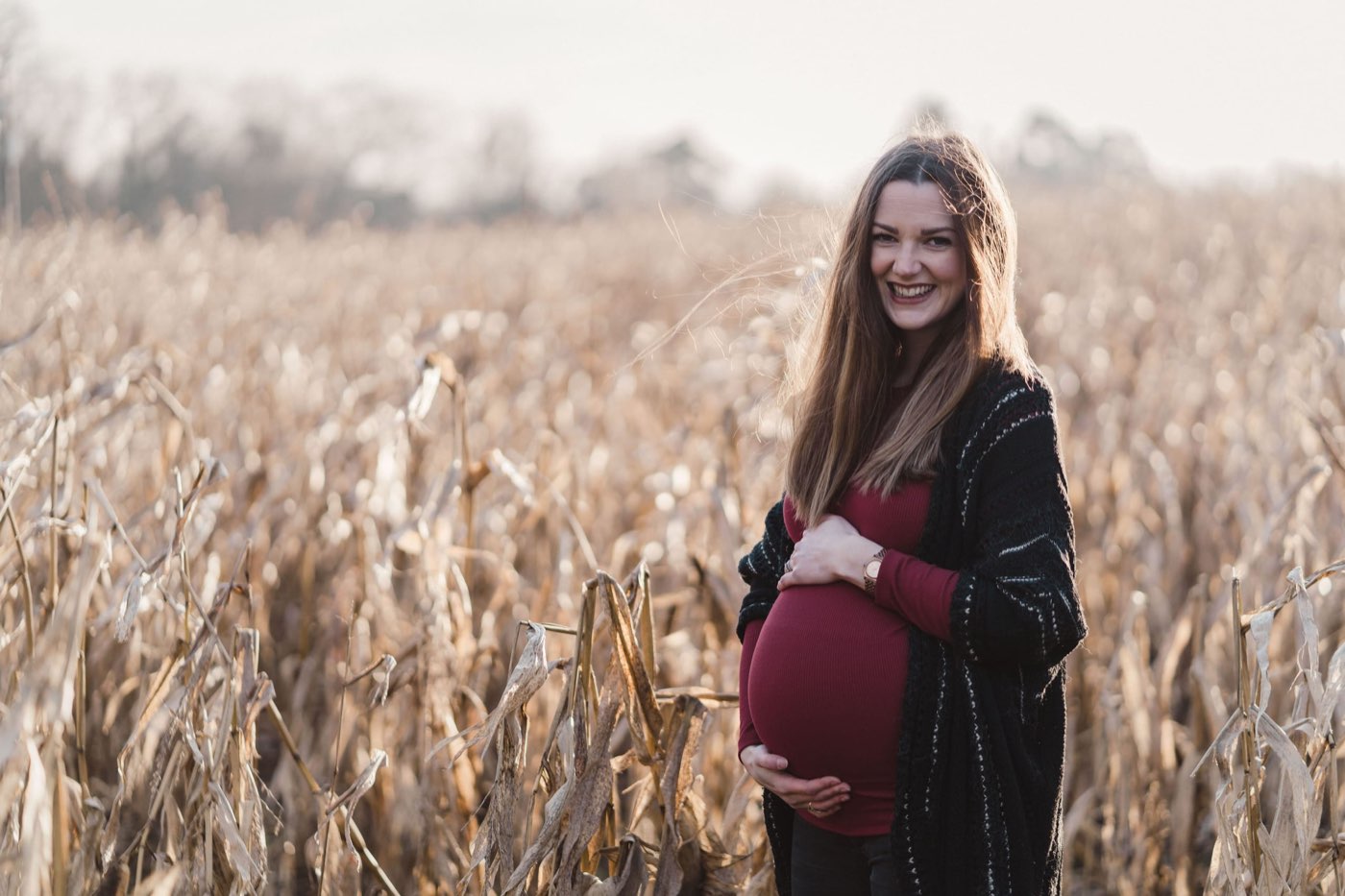 A pregnant woman standing in a golden corn field