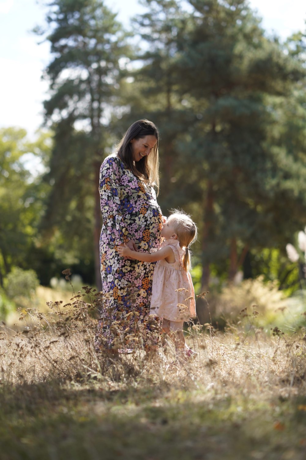 A pregnant mother and her daughter standing together in a meadow