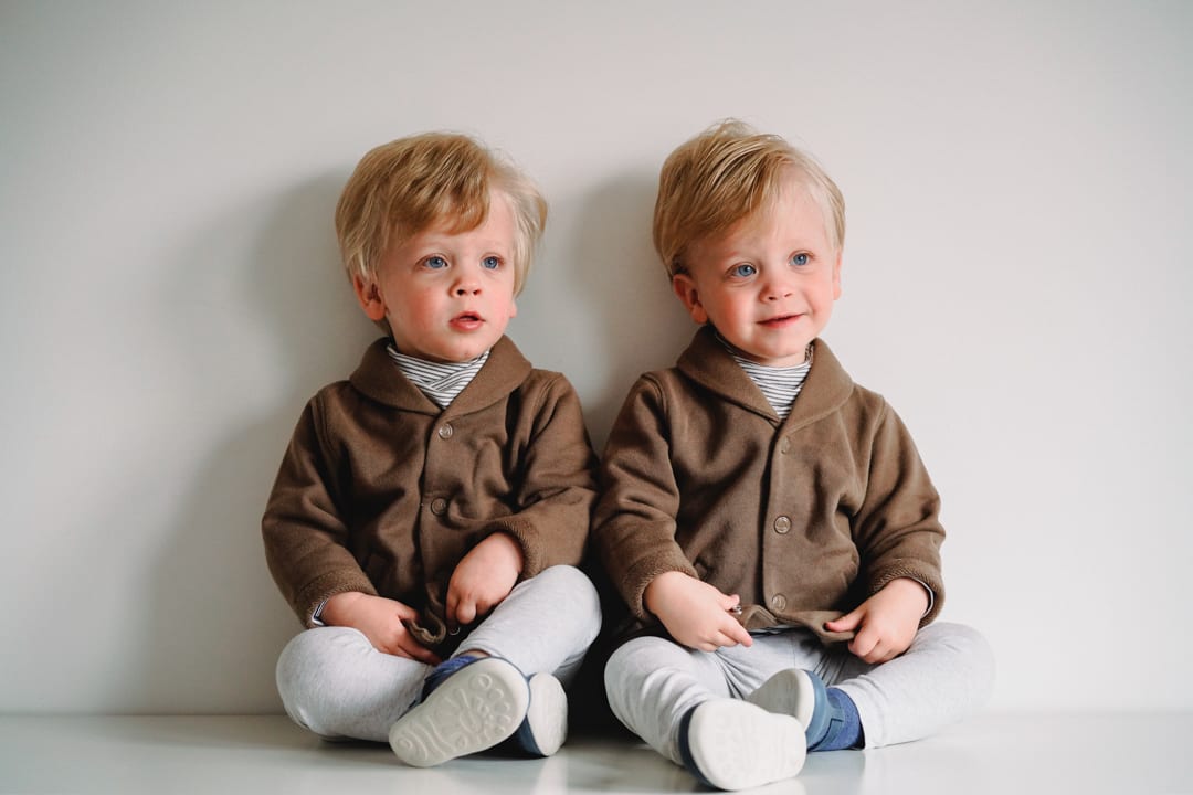 Twin boys sitting together against a plain studio wall